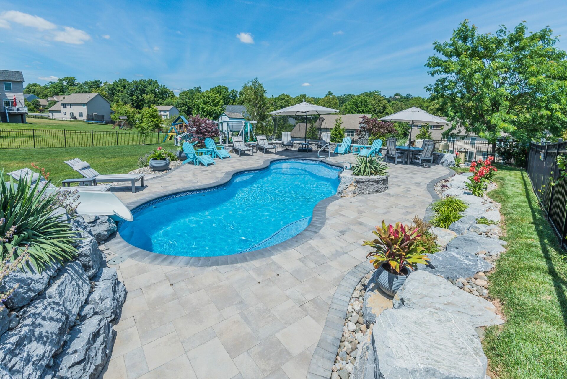 blue fiberglass pool with lounge chairs and potted plants