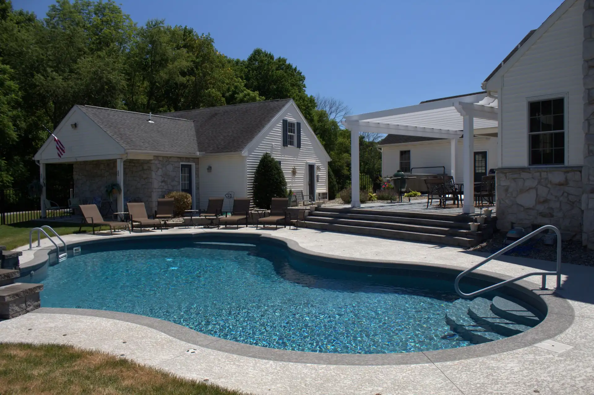 A curved inground pool with a jade liner sits in front of a white house on a sunny day. A darker-colored pool liner is one way you can improve the energy efficiency of your swimming pool.