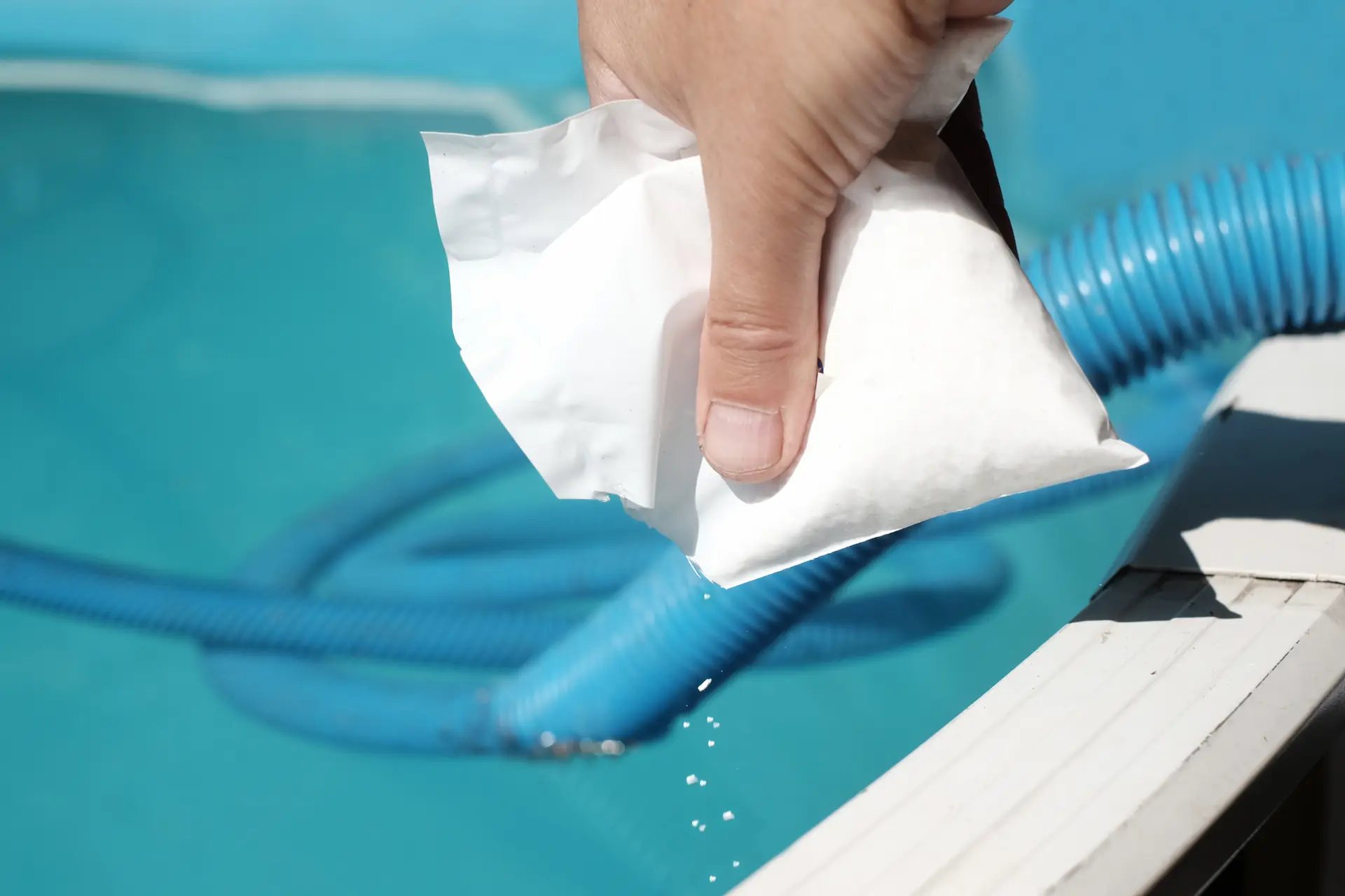 Closeup of a hand pouring powder chlorine from a bag into a pool. The form of the chemical is one reason why some pool chemicals cost more than others.