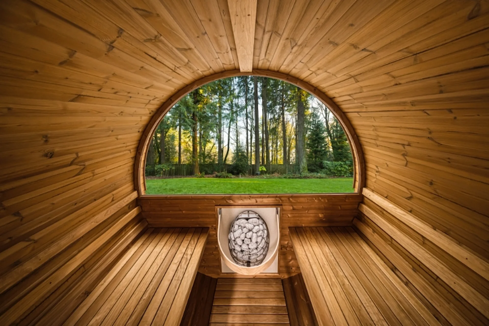 Interior shot of a barrel sauna with a view of a sunlit wooded area in the back window.